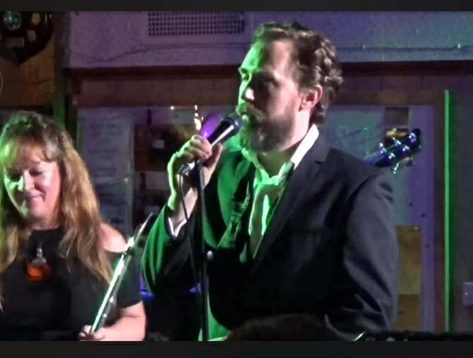Wade Morgan performing with green stage lighting and band